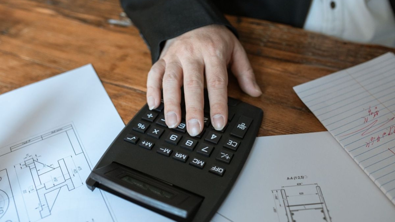 Hand on a calculator over interior drawings, checking BOQ quantities against the plans before an office fit-out